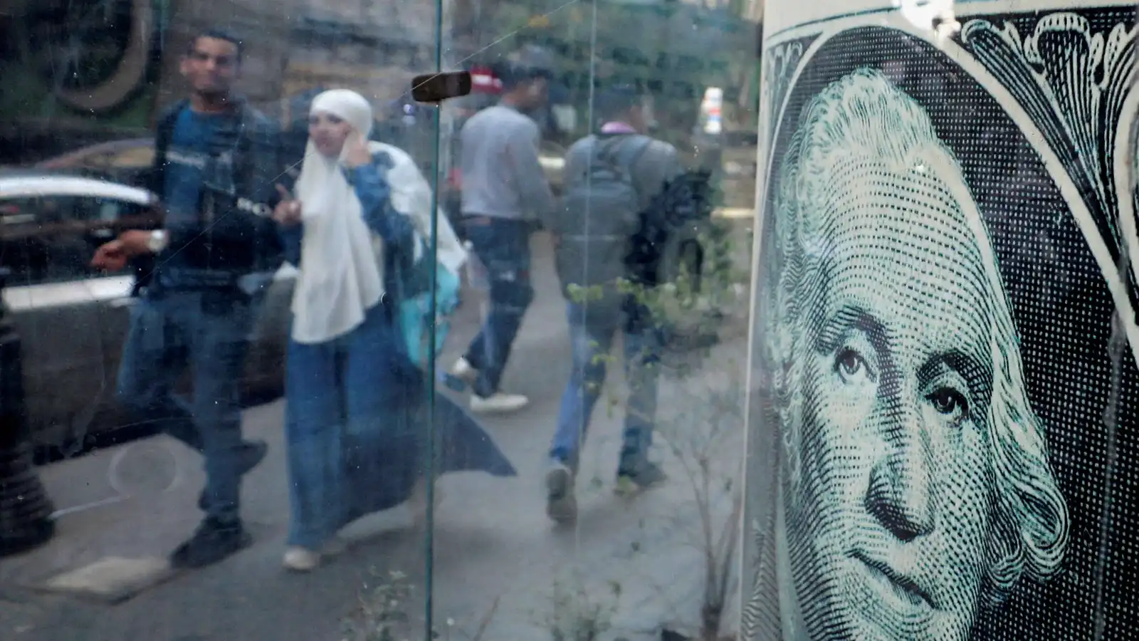 يمرون أمام مكتب صرافة يعرض صورة الدولار الأميركي، في العاصمة المصرية القاهرة، يوم 6 مارس 2024.