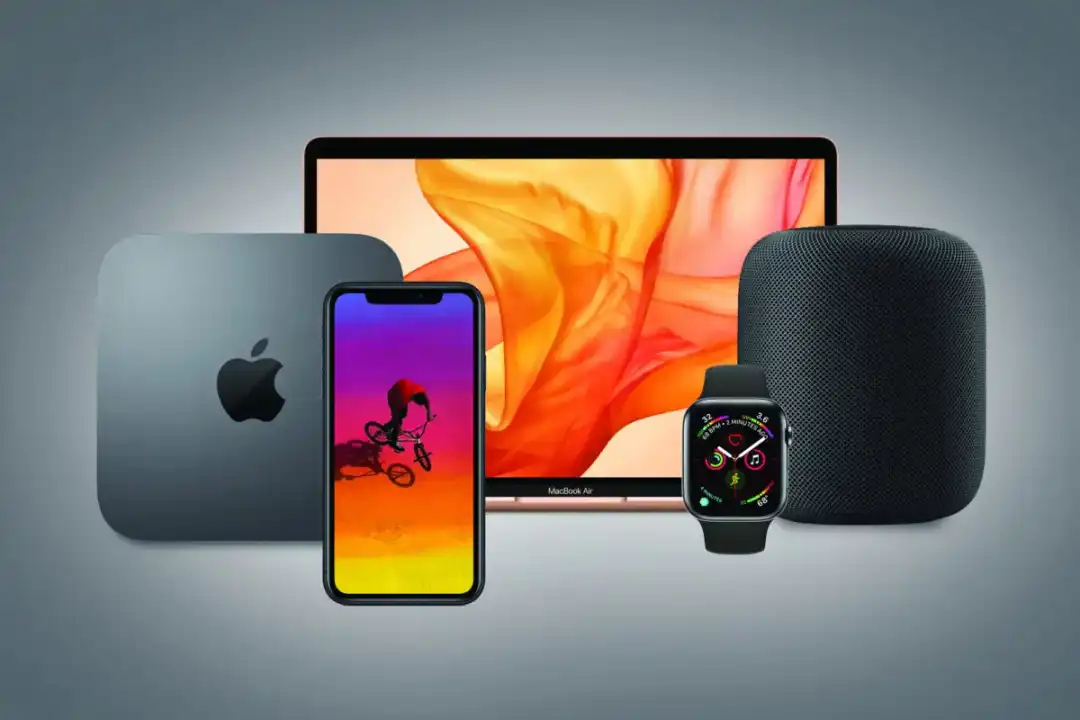 مجموعة من أجهزة Apple أمام خلفية رمادية ويظهر MacBook Air بشاشته المضيئة بألوان برتقالية وحمراء متداخلة.