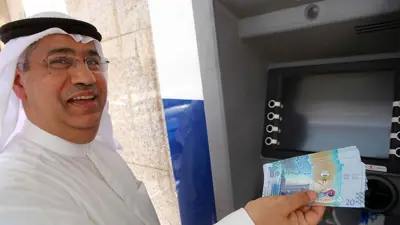 يحمل أوراقاً نقدية من فئة 20 ديناراً كويتياً بجوار ماكينة صراف آلي في مدينة الكويت يوم 29 يونيو 2014.
