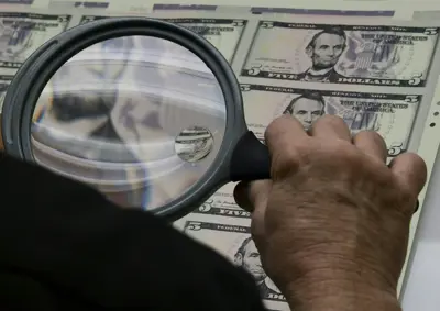موظف يتفحص أوراقاً نقدية من فئة 5 دولارات أميركية أثناء إخراجها من آلة الطباعة في مكتب النقش والطباعة التابع لوزارة الخزانة الأميركية في العاصمة واشنطن، يوم 20 يوليو 2018