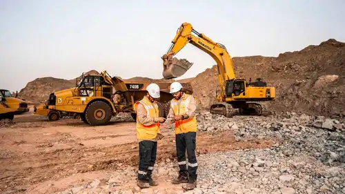 مهندسان يتابعان خطة العمل وسط آليات ثقيلة تعمل في موقع تعدين صخري، في سلطنة عُمان.
