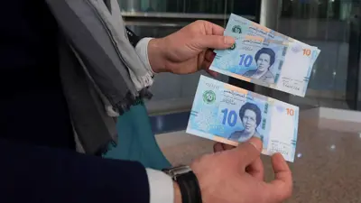 شخص يعرض أوراقاً نقدية تونسية متداولة حديثاً، داخل بنك في العاصمة تونس، في 27 مارس 2020.