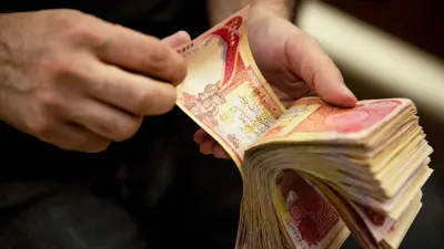 رزمة من الدنانير العراقية بيد أحد الصرافين، مدينة البصرة جنوبي العراق، يوم 12 ديسمبر 2023.
