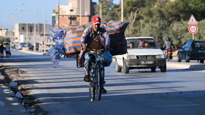 عامل جمع نفايات يقود دراجته محملة بزجاجات بلاستيكية مُنتشلة من حاويات القمامة في منطقة أريانة قرب تونس العاصمة، 10 يوليو 2025.