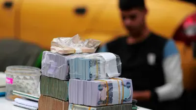 صراف أمامه مجموعة من الدنانير العراقية والعملات الأجنبية في مكتب صرافة في العاصمة بغداد، يوم 12 ديسمبر 2023