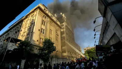 يراقب الناس رجال الإطفاء وهم يُخمدون النيران بعد اندلاع حريق في سنترال رمسيس بقلب القاهرة