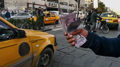 يلوح برزمة من أوراق العملة السورية من فئة الـ2000 ليرة في أحد شوارع العاصمة السورية دمشق يوم 14 يناير 2025.