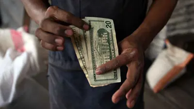 يمسك أوراقاً نقدية من الدولار الأميركي بمتجر حبوب في العاصمة السلفادورية سان سلفادور يوم 22 مايو 2024.