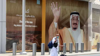  حاج يرتدي ملابس بيضاء يمر أمام صورة ملك السعودية سلمان بن عبد العزيز في مطار الملك عبد العزيز يوليو 2021