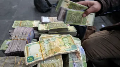 تاجر عملة يجلس بجوار كومة من الليرات السورية في كشكه في أحد شوارع دمشق في 14 يناير 2025