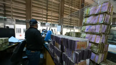 يقف موظف البنك بجانب رزم من الأوراق النقدية السورية بينما يخدم العملاء في بنك تجاري تابع للبنك المركزي السوري في دمشق، 16 ديسمبر 2024.