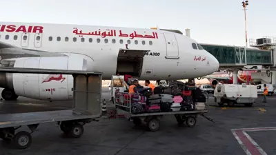 عاملان ينقلان أمتعة بجوار طائرة تابعة للخطوط الجوية التونسية، في مطار قرطاج الدولي في تونس، يوم 19 يوليو 2016.